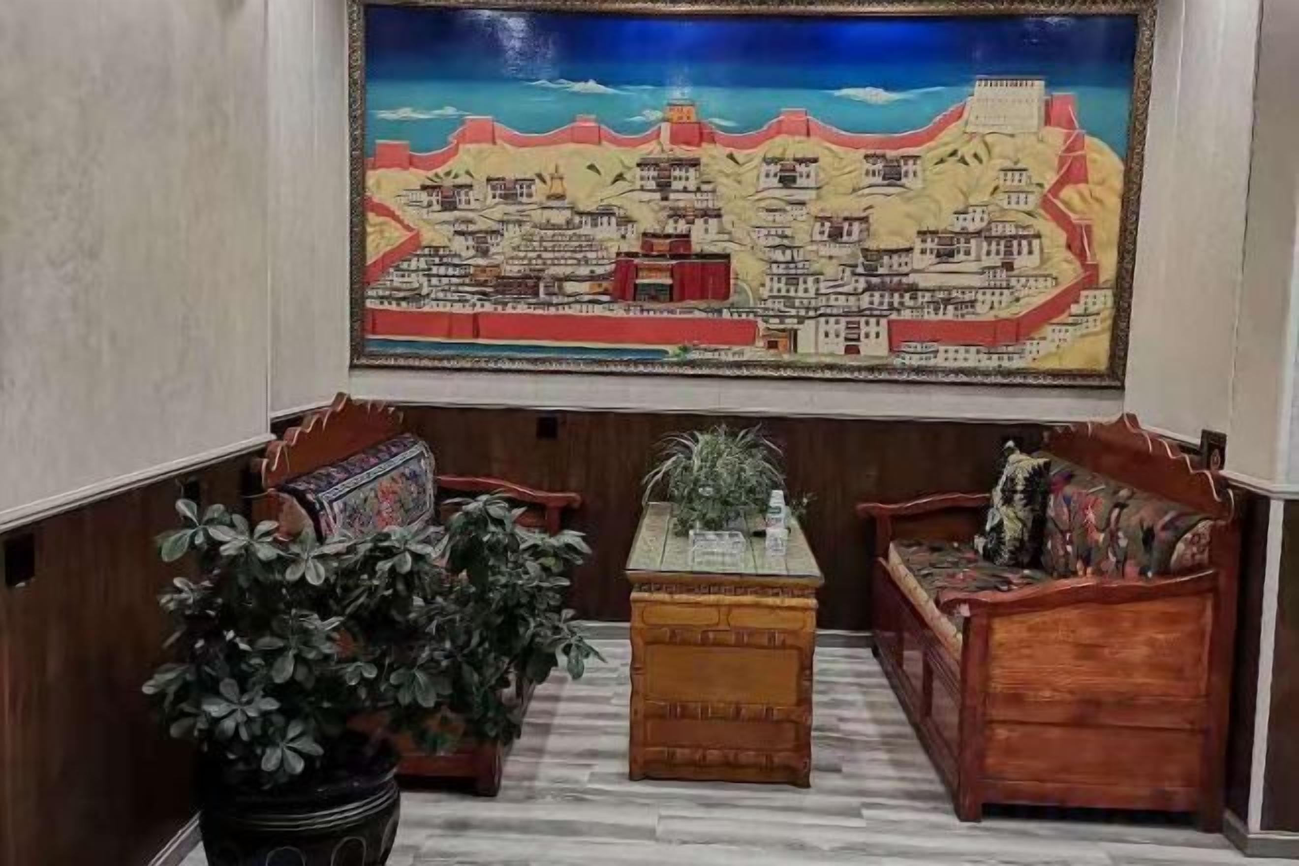A room with a large wall painting, a wooden bench, a small table with a plant, and a potted plant.