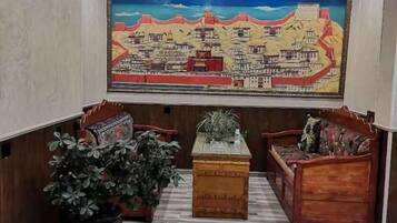 A room with a large wall painting, a wooden bench, a small table with a plant, and a potted plant.