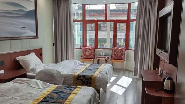A hotel room with two beds, a TV, a desk, and a window with curtains. - Gaji Hotel (Gyantse)