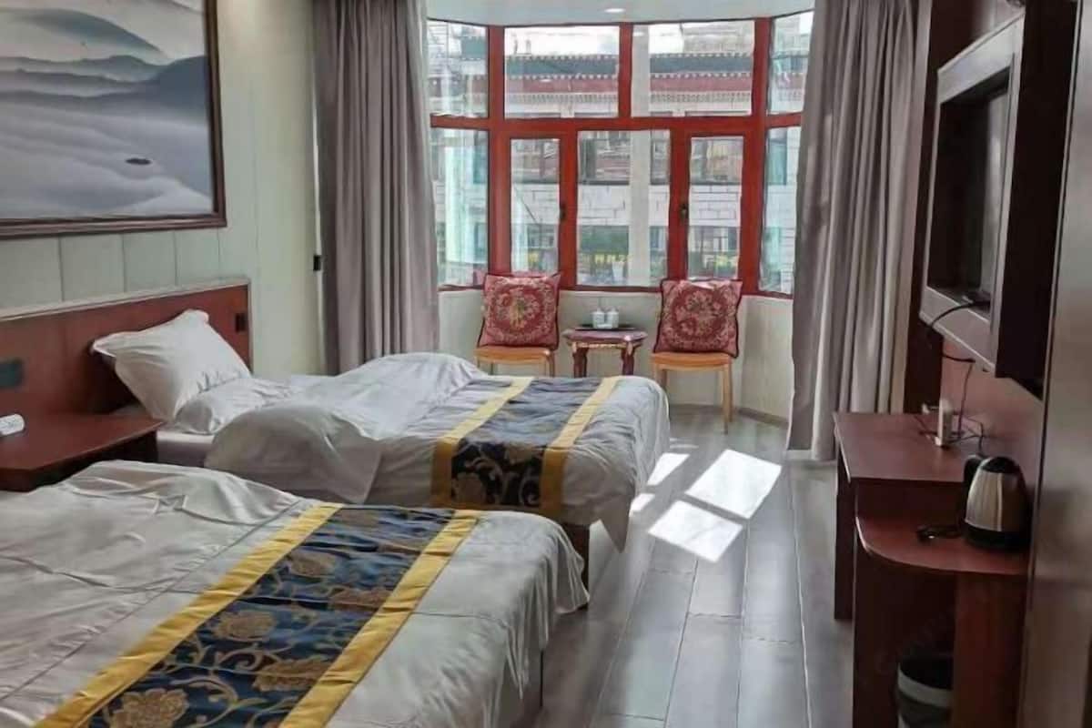 Ein Hotelzimmer mit zwei Betten, einem Fernseher, einem Schreibtisch und einem Fenster mit Vorhängen.