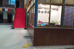 A staircase leading to an upper level, a reception desk with a window, and a colorful wall pattern. - Gaji Hotel (Gyantse)