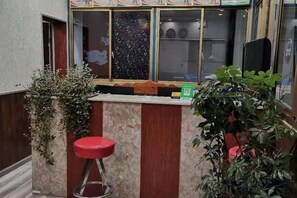 A small reception area with a wooden counter, a red stool, and a potted plant. - Gaji Hotel (Gyantse)