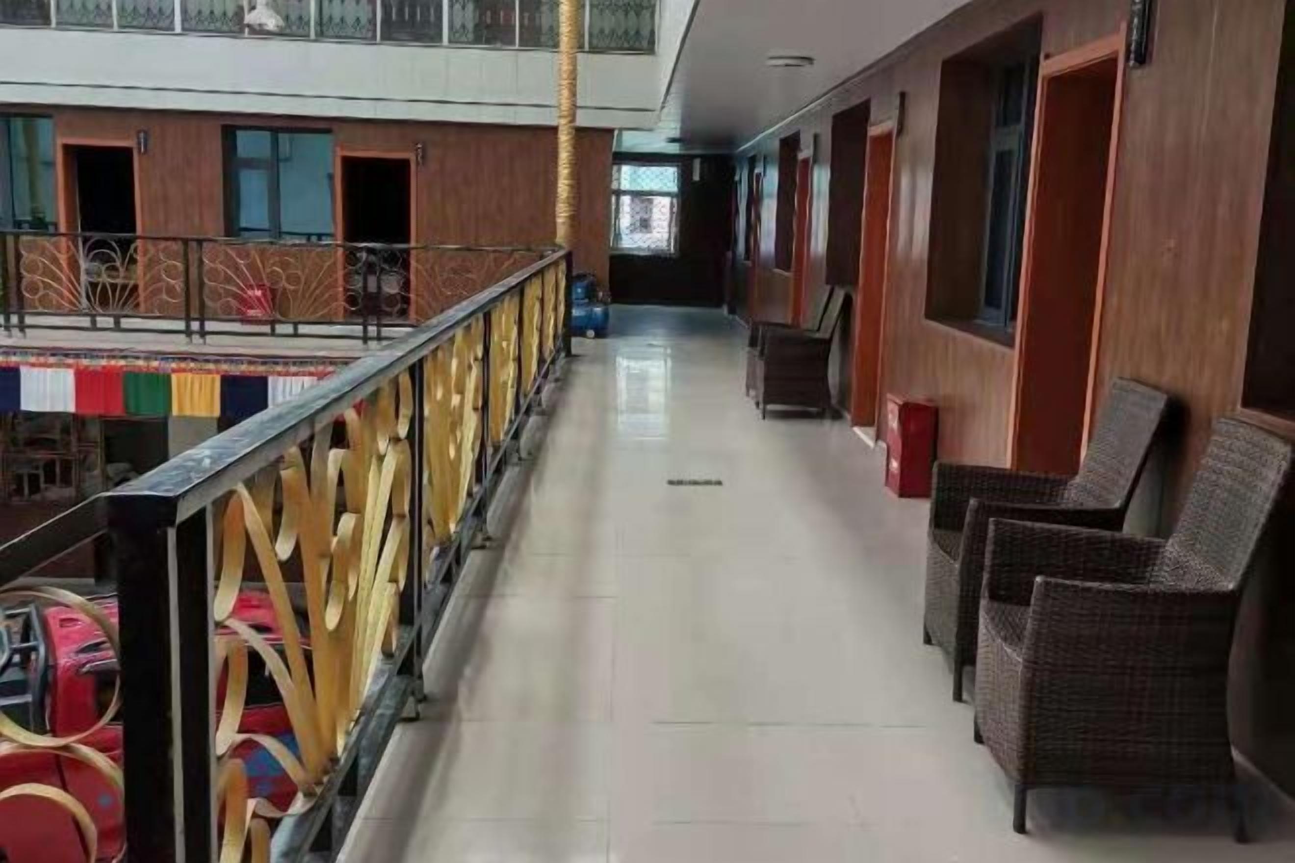 A hotel corridor with wicker chairs, a railing, and a view of the pool area.