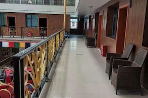 A hotel corridor with wicker chairs, a railing, and a view of the pool area.
