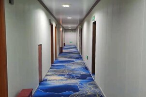 Un pasillo de hotel con alfombra estampada, puertas a ambos lados y un banco al final.