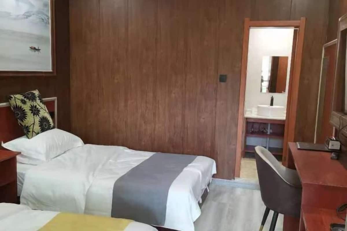 Ein Hotelzimmer mit einem Bett, einem Schreibtisch, einem Stuhl, einem Spiegel und einem durchgegangene Tür erkennbaren Badezimmer.