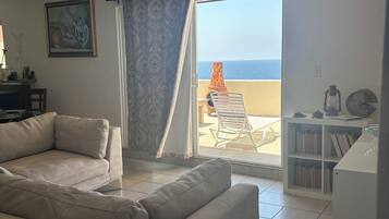 Una sala de estar con un sofá color crema, un cuadro y vista al mar a través de un ventanal corredero.