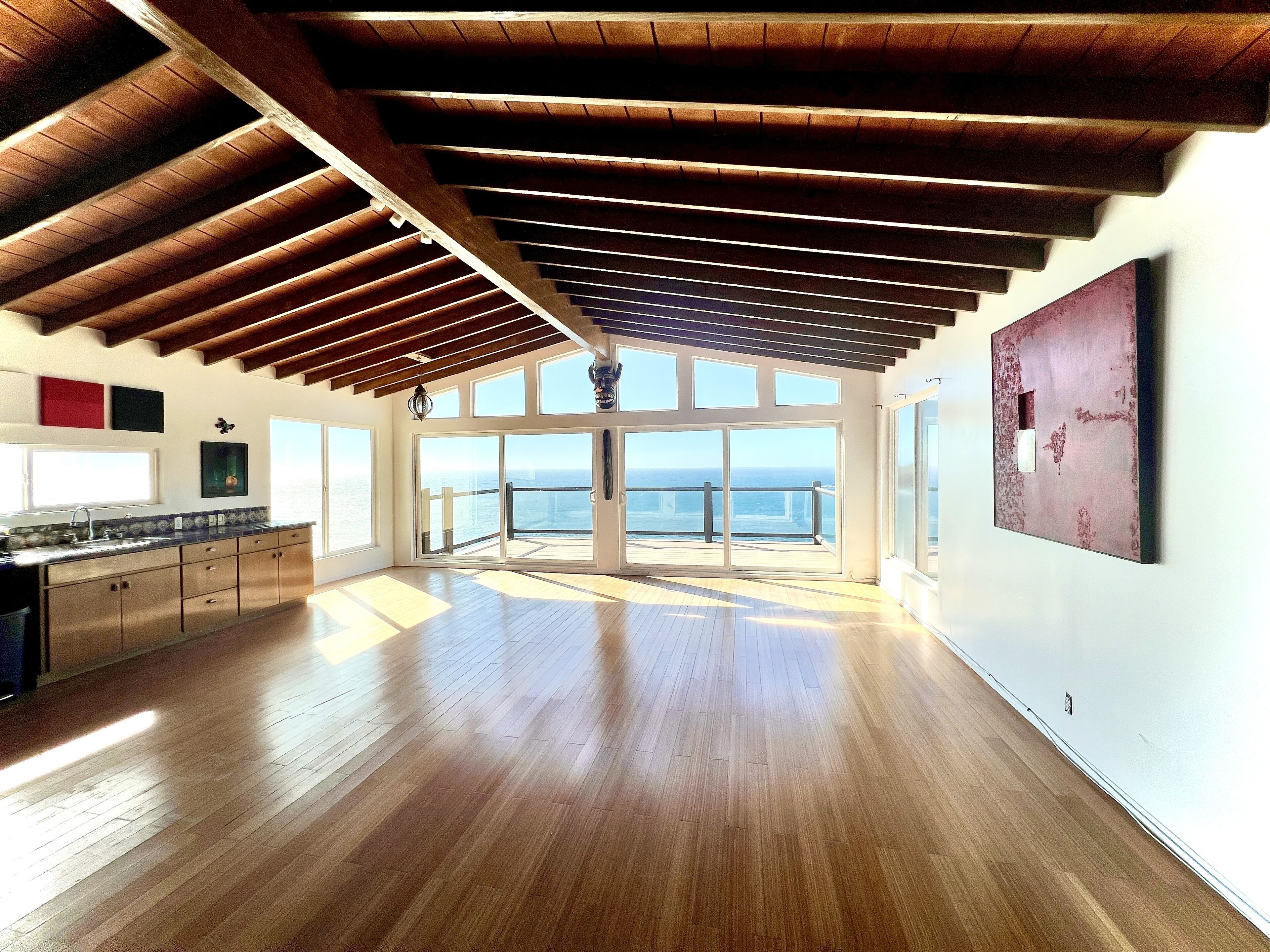 A spacious room with a wooden floor, large windows, and a view of the ocean.