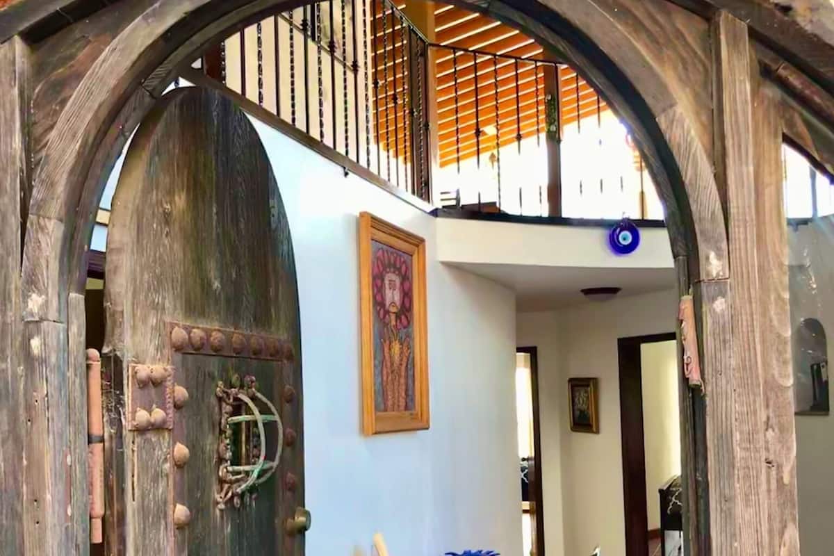 An arched wooden door with a rustic design, leading to a room with a patterned carpet and a table with papers.