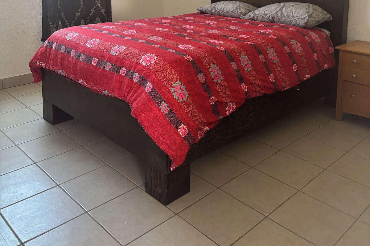 A bedroom with a bed, a nightstand, a window with curtains, and a tiled floor.