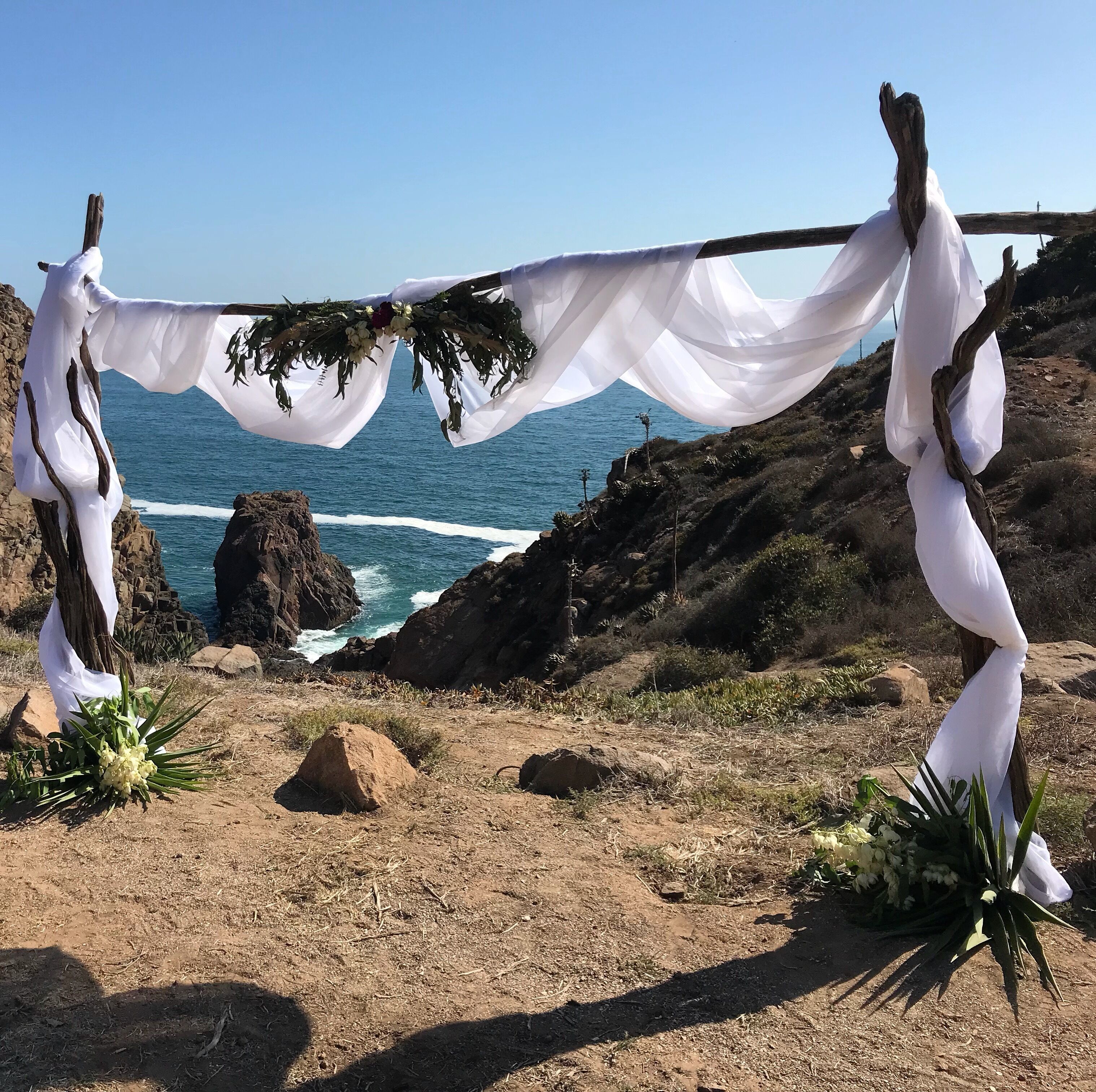 Een kustlandschap in de open lucht, met een wit kleed over een houten constructie, mogelijk onderdeel van een ceremonie of evenement.
