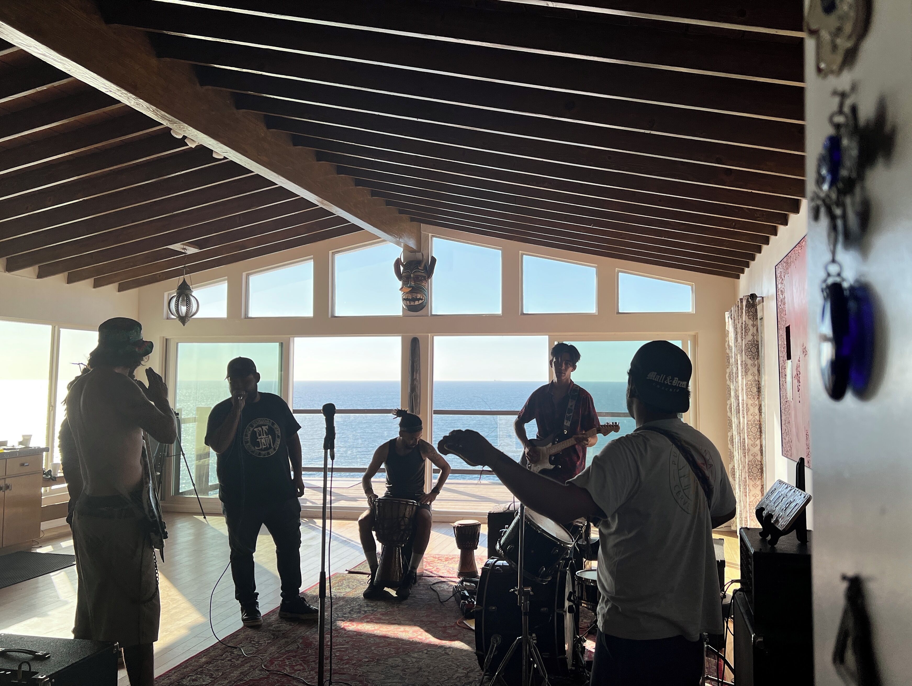 A spacious room with large windows overlooking the sea, a drum set, and a microphone stand.