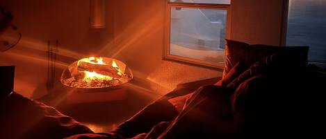 Una habitación acogedora con chimenea, una ventana con vista al cielo y una cama con almohadas.