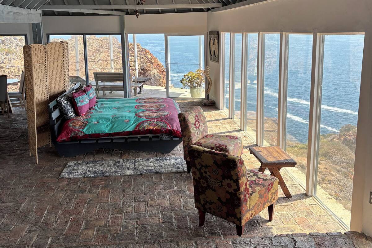 A room with a bed, a chair, and a view of the ocean.