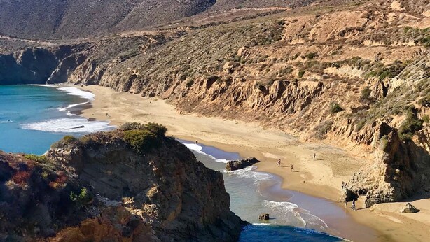 A coastal landscape with rocky cliffs, a sandy beach, and clear blue waters. - Baja Off the Grid, Luxury Nature Glamping Retreat (Cabo Punta Banda)