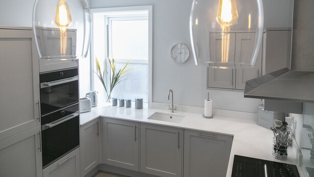 Une cuisine moderne avec deux luminaires suspendus, une fenêtre, un évier et une horloge au mur.