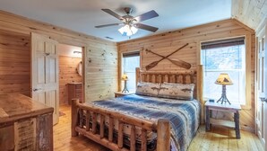 A rustic wooden cabin bedroom with a bed, a ceiling fan, a window with a view, and a wooden dresser. - Bearfoot's Nantahala Retreat-Pastoral View - Internet - Pool table - Fire Pit (Bryson City)