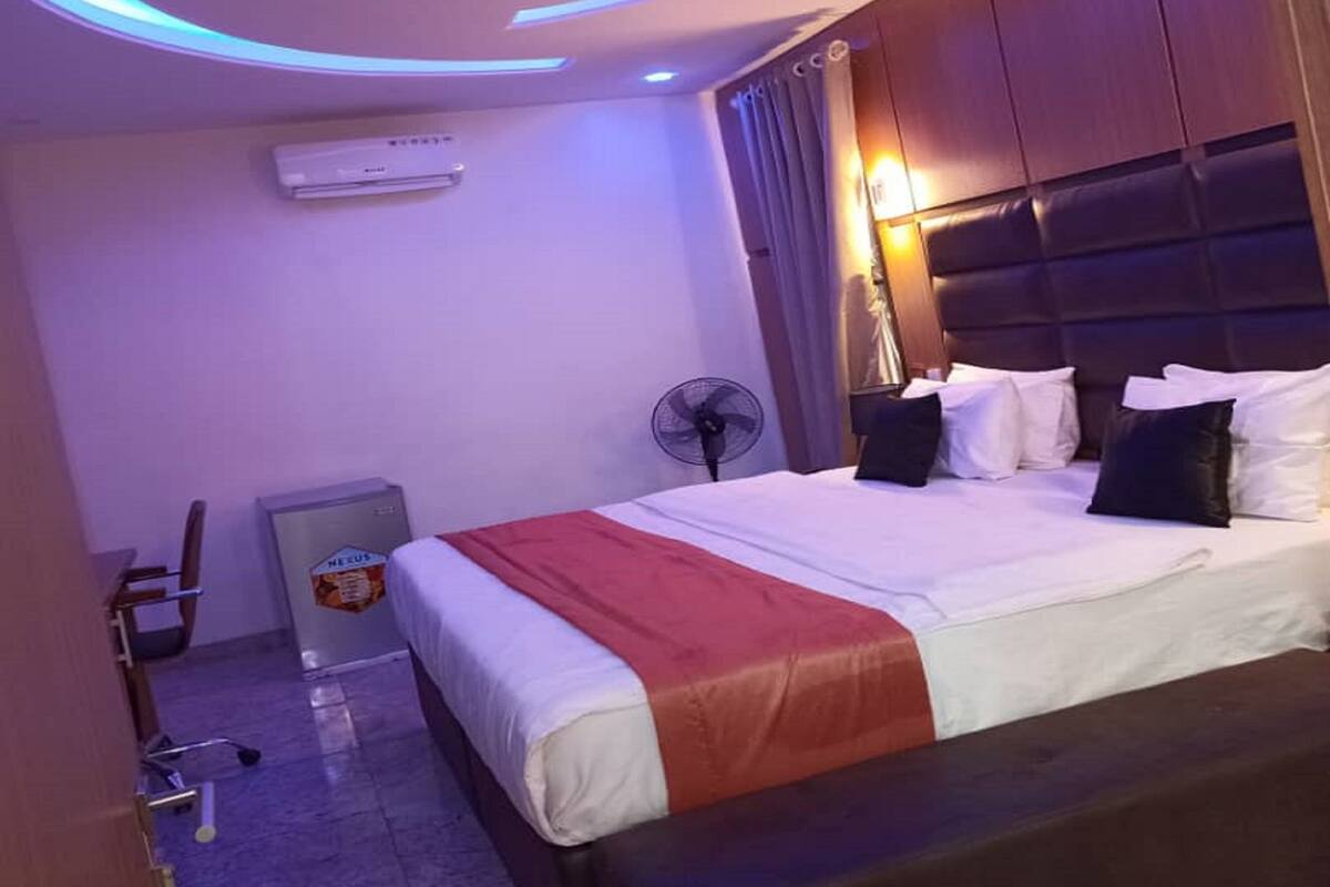 Quarto de hotel com cama, mesa de cabeceira, ventoinha, ar condicionado e um pequeno armário.