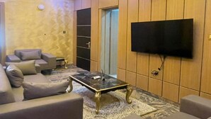 Ein Wohnzimmer mit einem an der Wand befestigten Flachbildfernseher, einer Decke mit einer runden Leuchte und einer Sofagarnitur.