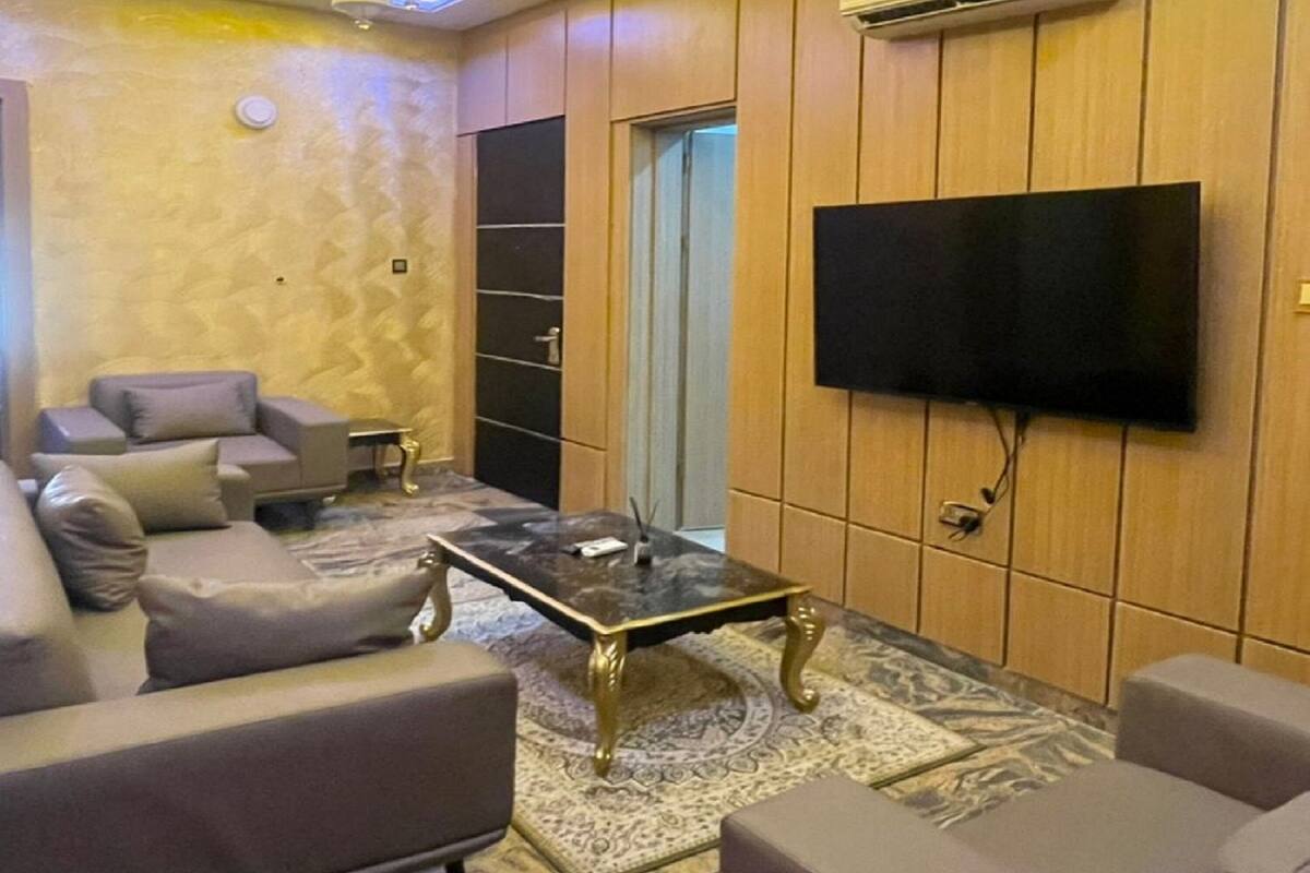 Uma sala de estar com televisão de tela plana na parede, luminária circular no teto e um conjunto de sofás.