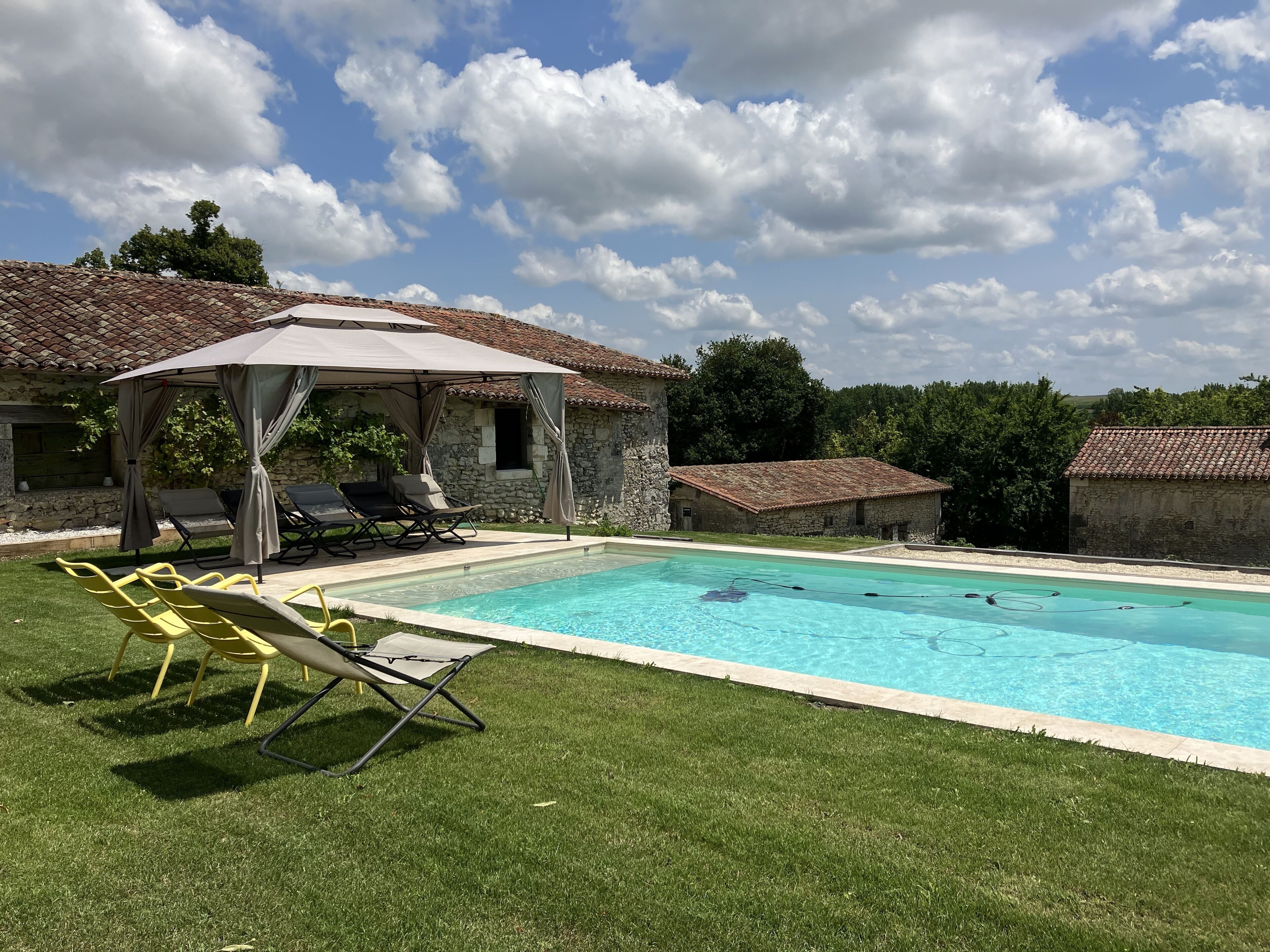 A swimming pool with lounge chairs and a covered area, surrounded by stone buildings and greenery.