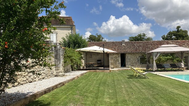 Un bâtiment en pierre avec un toit en tuiles, une piscine et un espace extérieur aménagé pour s’asseoir.