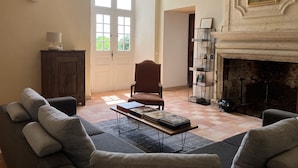 Un salon comprenant un canapé, des fauteuils, une table basse avec des livres, une cheminée et une bibliothèque.