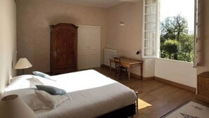 Une chambre à coucher comprenant un lit, un bureau, une chaise, une armoire et une fenêtre donnant sur un paysage verdoyant.