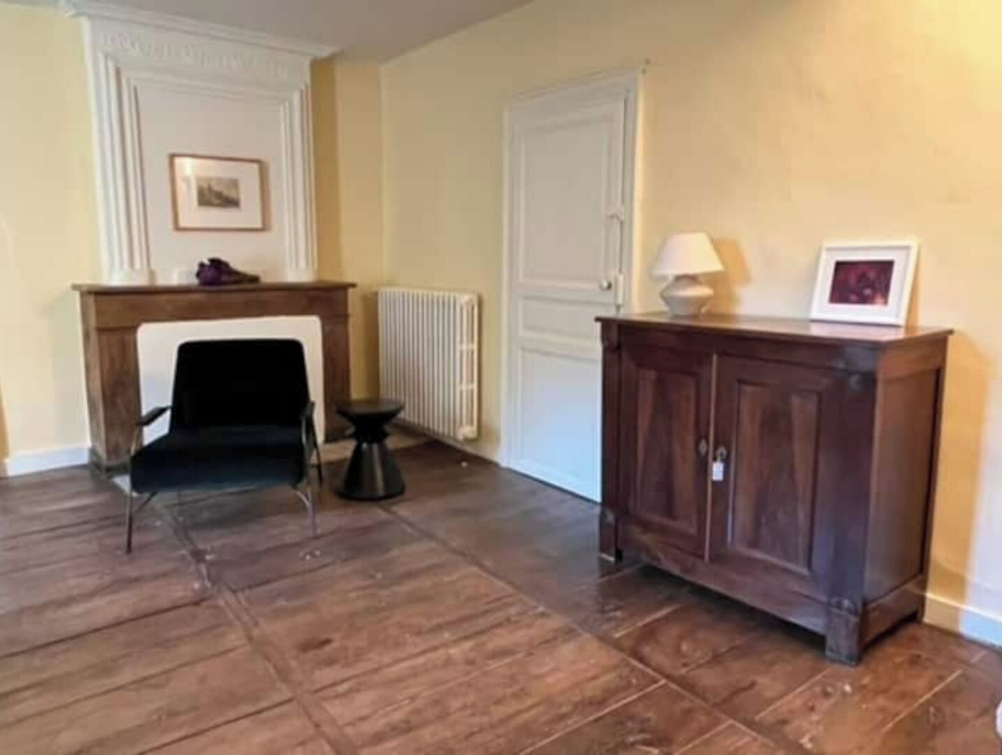 Una habitación con chimenea, una silla negra, un armario de madera y un radiador.