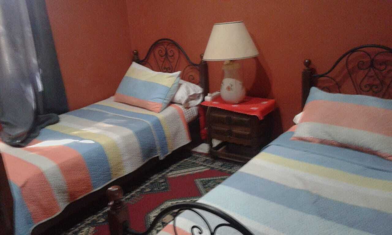 Una habitación con dos camas, cada una con ropa de cama a rayas, una mesita de noche con lámpara y una alfombra estampada.