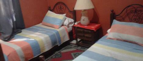 Una habitación con dos camas, cada una con ropa de cama a rayas, una mesita de noche con lámpara y una alfombra estampada.