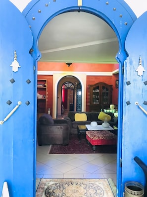 An interior view through a blue arched doorway leading to a living room with a sofa, armchairs, and a coffee table.