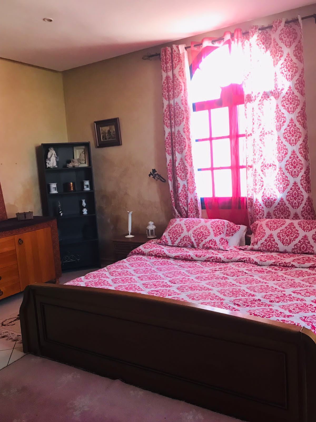 A bedroom with a bed, a dresser, a nightstand, and a window with curtains.