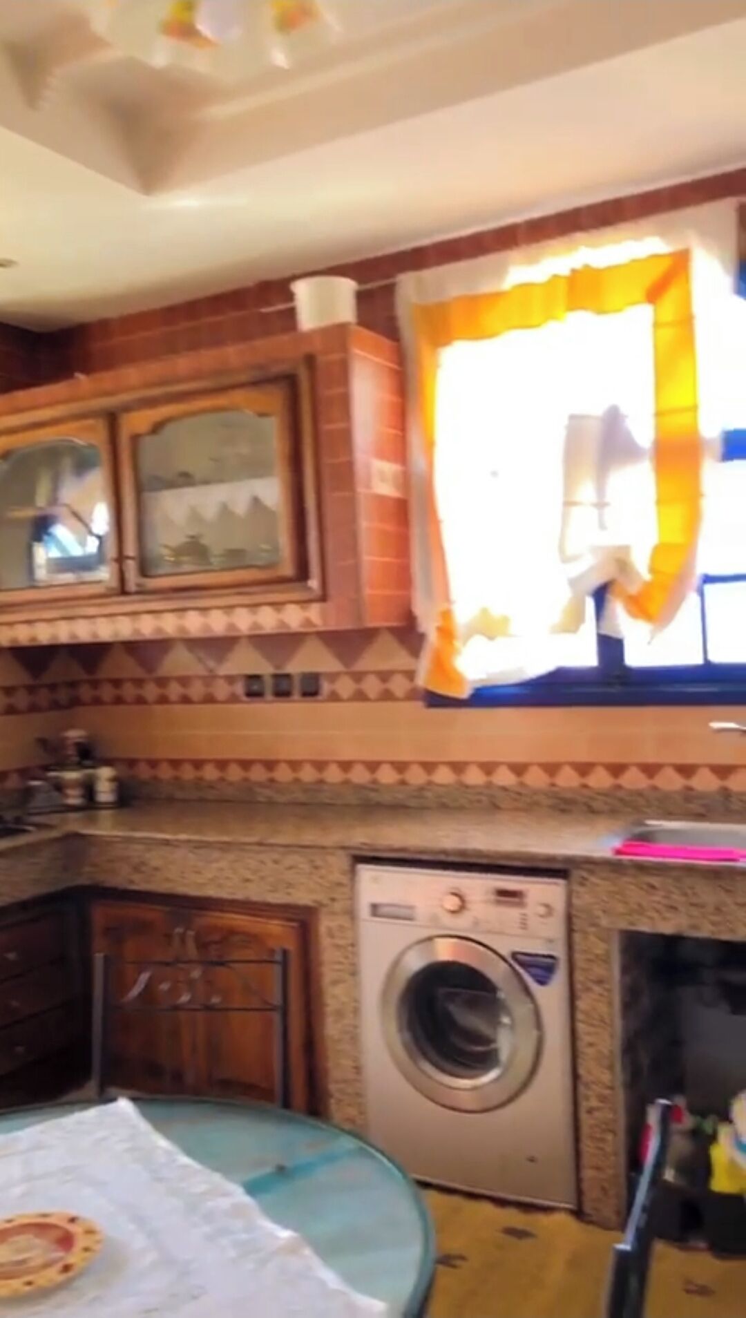 Een keuken met houten kastjes, een wasmachine en een raam met gordijnen.