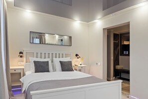 A modern bedroom with a white bed, bedside tables, a nightstand, a mirror, and a walk-in closet.