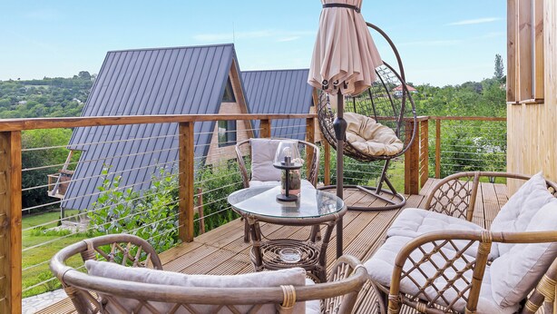 Eine Holzterrasse mit Korbmöbeln, einem Glastisch und einem Hängesessel.