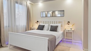 Ein Schlafzimmer mit einem weißen Bett, zwei Nachttischen, einem Schminktisch und leichten Vorhängen.