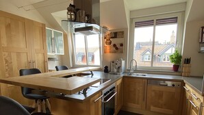 Una cocina moderna con armarios de madera, horno empotrado, cafetera y ventana con vistas a edificios.