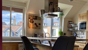 Una cocina moderna con una isla central, taburetes de madera, horno empotrado y vistas a la ciudad a través de amplias ventanas.