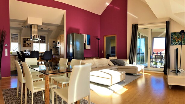 Una sala moderna con una mesa de comedor de vidrio, sofás blancos y una cocina al fondo.