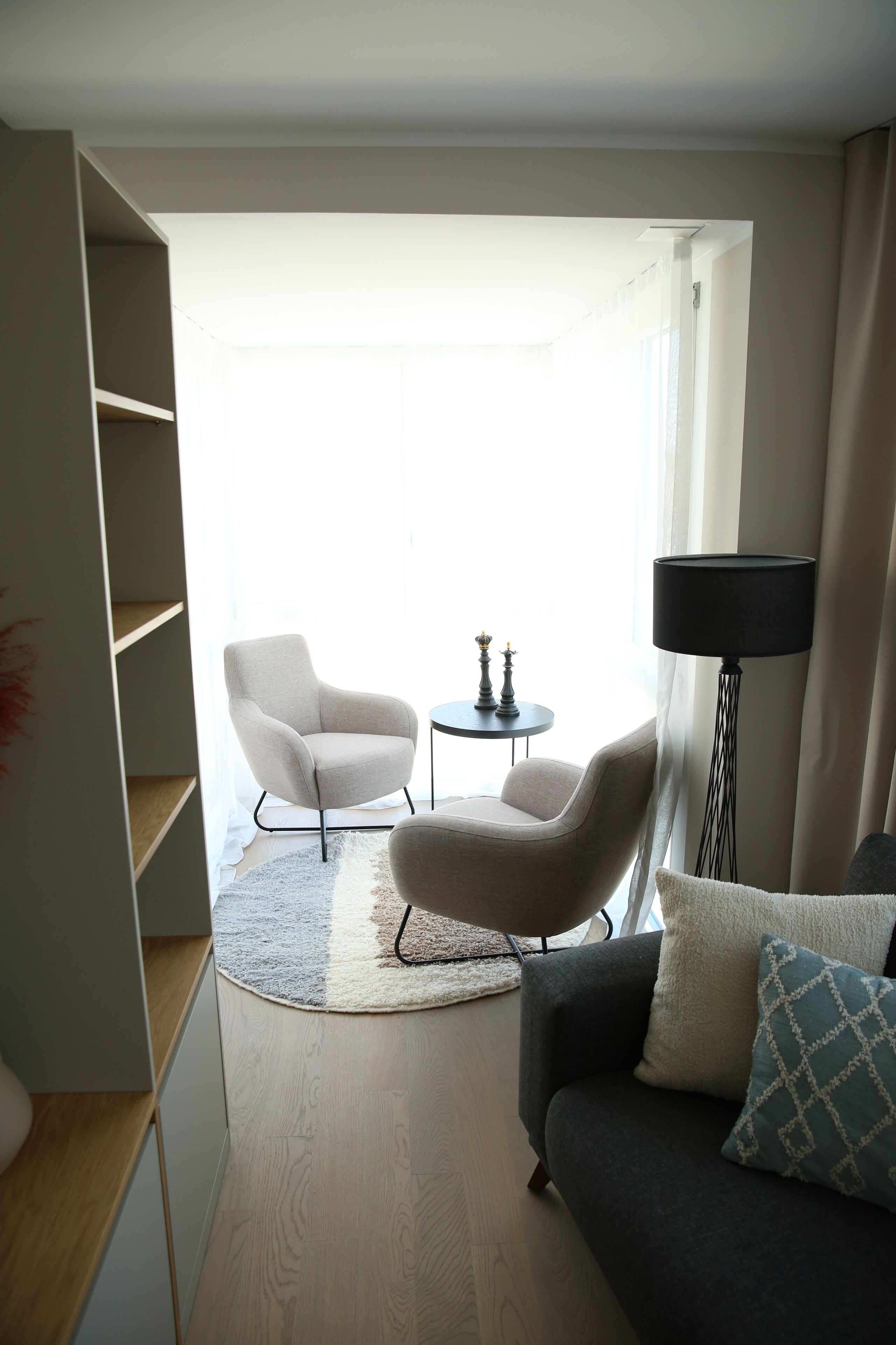 A modern living room with a grey sofa, a white armchair, a small round table with two decorative items, and a floor lamp.