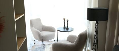 A modern living room with a grey sofa, a white armchair, a small round table with two decorative items, and a floor lamp.