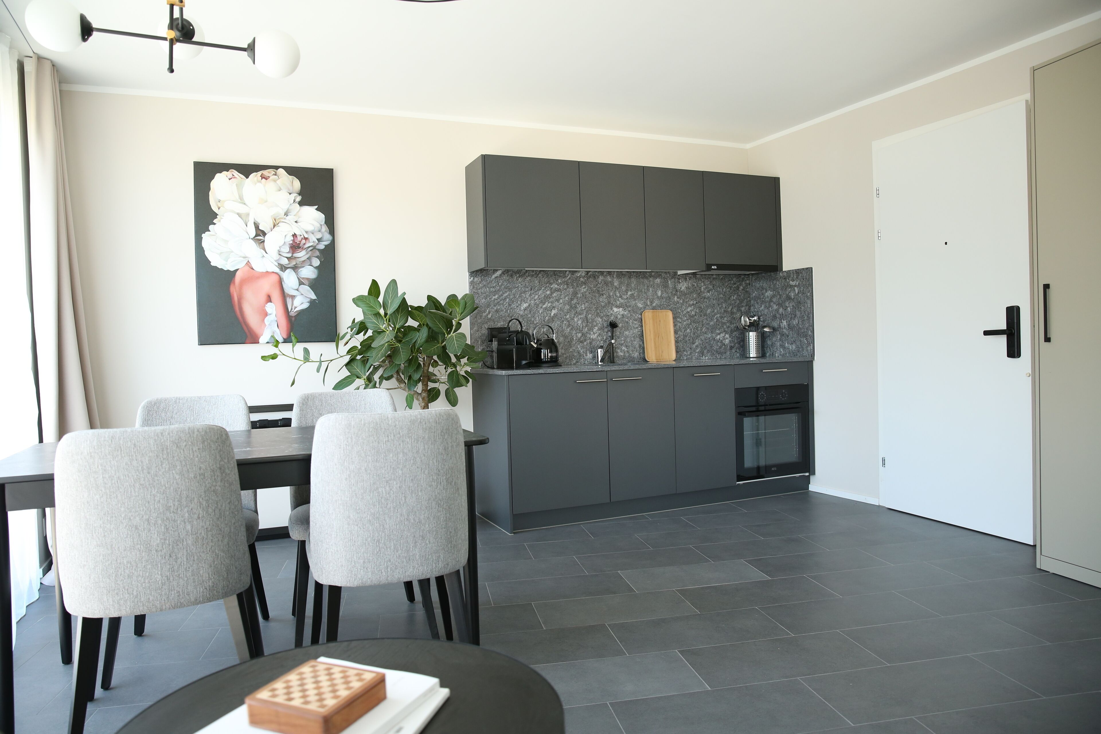 Une cuisine moderne avec des meubles gris, un plan de travail en marbre et un coin repas comprenant une table et des chaises.