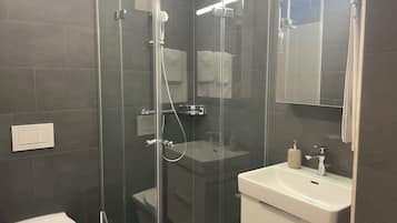 Ein modernes Badezimmer mit einer Duschkabine, einem weißen Waschbecken und einer Toilette.