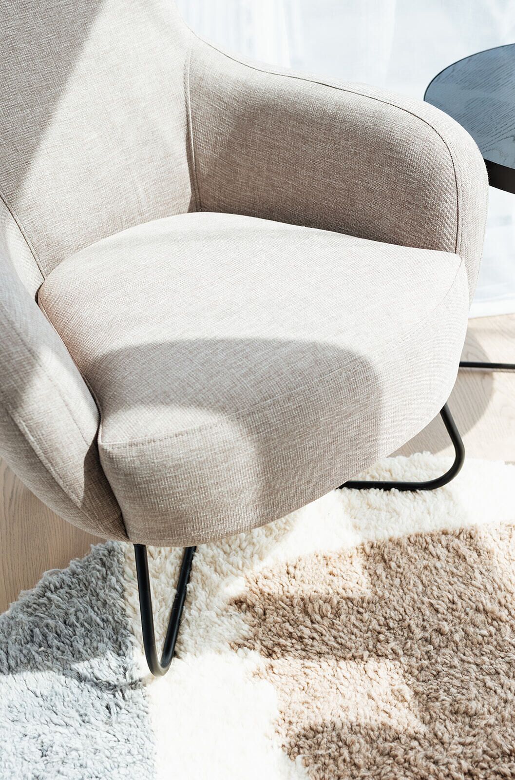 Un fauteuil beige aux pieds en métal noir, placé sur un tapis à motifs.