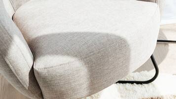 Un fauteuil beige aux pieds en métal noir, placé sur un tapis à motifs.