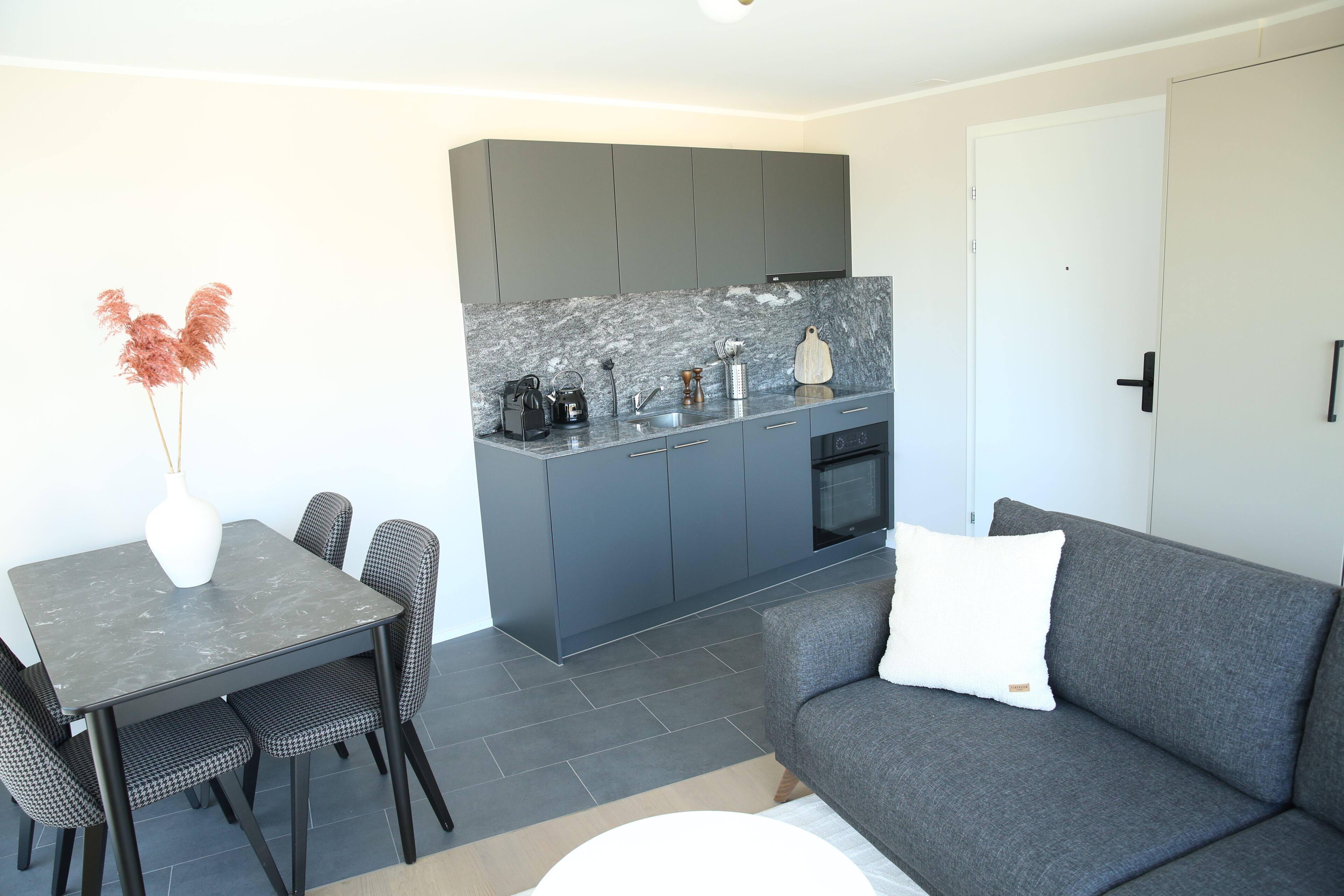 A modern kitchen with grey cabinets, a marble countertop, and a dining area with a table and chairs.