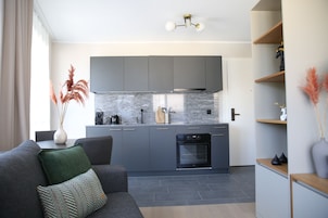 A modern kitchen with grey cabinets, a built-in oven, and a stone backsplash.