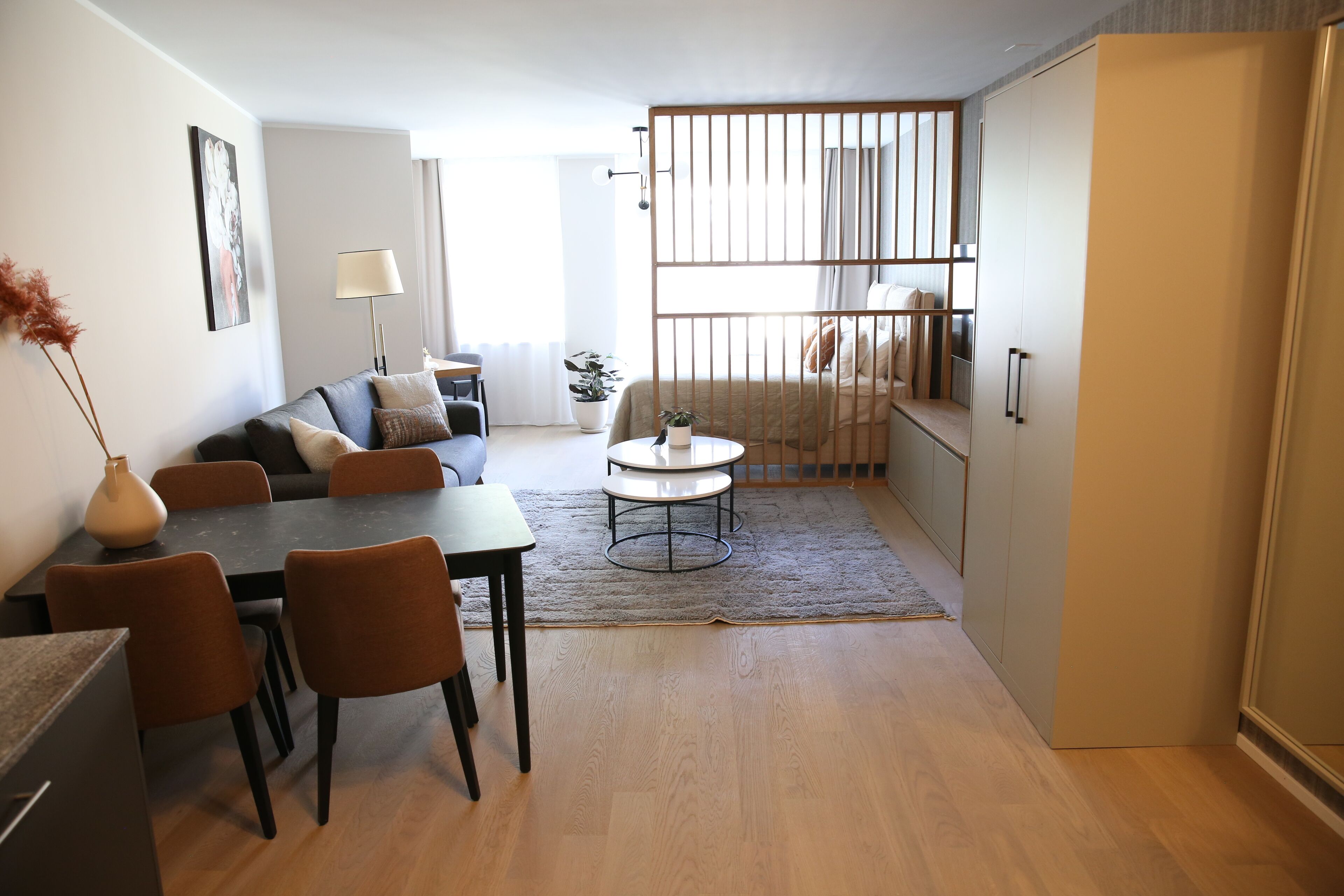 Una sala moderna con sofá, mesa de comedor, sillas y una mesita de centro. Se observa también una zona de cocina con armarios y un refrigerador.