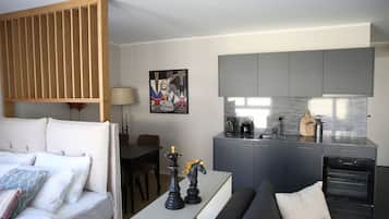 A modern living room with a sofa, a dining table, and a kitchen area with grey cabinets and a built-in oven.